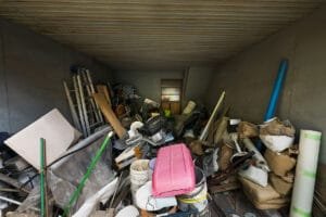 Cluttered storage room filled with junk, tools, buckets, and miscellaneous household items.