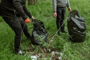 Two people cleaning up litter in a grassy area, filling large black garbage bags.