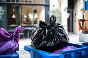 Black and purple garbage bags placed inside blue recycling bins on a city street.