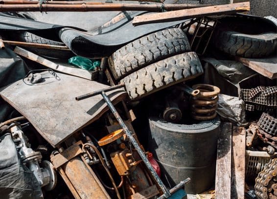 Pile of scrap metal, tires, and car parts in a junkyard or recycling facility.
